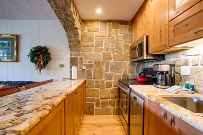 a kitchen with wooden cabinets and a stone wall at Pool and 3 Hot Tubs Winter Park Condo on Bus Line in Winter Park