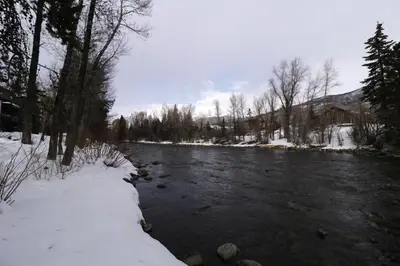 a river with snow on the banks and trees at River West 611 condo in Silverthorne