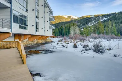 a house with snow on the ground next to a river at Steps to River Run Gondola Ski Condo with Views! in Keystone