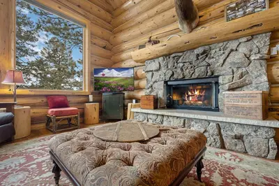 a living room with a stone fireplace in a log cabin at Mounticello Log Cabin - Relaxing Front Patio & Outdoor Firepit in Estes Park