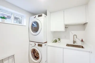 a white kitchen with a washer and dryer next to a sink at Less Than 1 Block to City Park New-Build Apt in Denver! in Denver