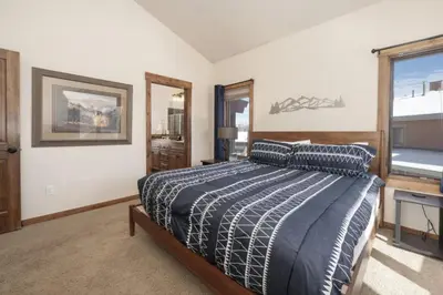 a bedroom with a bed with a blue comforter and a window at Hot Tub Mountain Views Steps to Trails in Winter Park