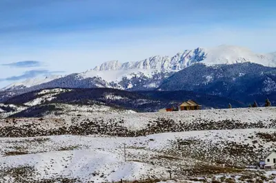 a house on a snowy hill with mountains in the background at Luxe MTN Escape 15 min to Winter Park Base in Tabernash