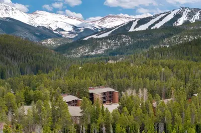a building in the middle of a forest with snow covered mountains at Winter Park Chalet I Mtn Biking I Summer festivals in Winter Park