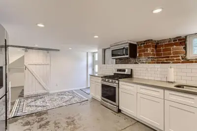 a kitchen with white cabinets and a brick wall at A Pet Friendly And Remodeled I Near RiNo Where Sleeps 7 in Denver