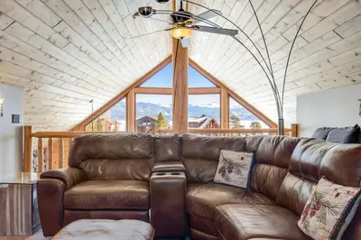 a living room with a leather couch and a ceiling fan at Granby Modern Cabin - Hot Tub & Mountain Views in Granby