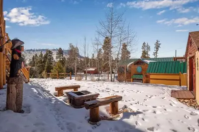 a snow covered yard with a bench and a building at Granby Modern Cabin - Hot Tub & Mountain Views in Granby