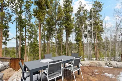 a table and chairs with trees in the background at Luxe & Leisure in Fairways- An Oasis in the Woods in Granby