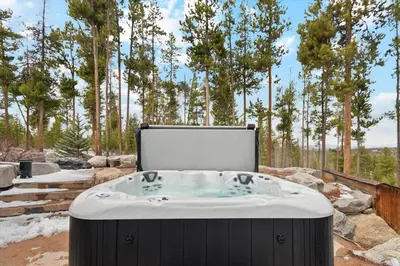a hot tub in a field with trees in the background at Luxe & Leisure in Fairways- An Oasis in the Woods in Granby