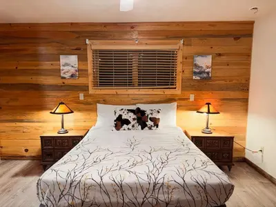 a bedroom with wooden walls and a bed with two lamps at Grand Lake Haven in town, Osprey Studio Cabin in Grand Lake