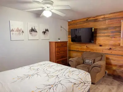 a bedroom with a bed and a tv and a chair at Cozy cabin Steps from Lake and Board walk, 5 min RMNP, Moose Lodge Studio in Grand Lake