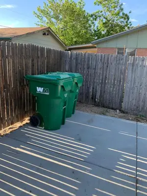two green trash cans sitting next to a fence at Bright basement unit with large yard and sunroom in Denver