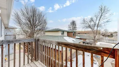 a house with a wooden balcony with snow on the ground at Convenient two bedroom near DIA in Brighton