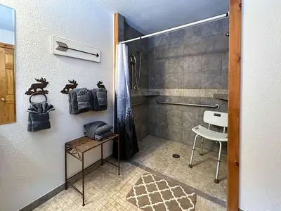 a bathroom with a shower and a chair in it at Kinnikinnick Retreat Steps from the Lake and Board walk, 5 min drive to RMNP. in Grand Lake