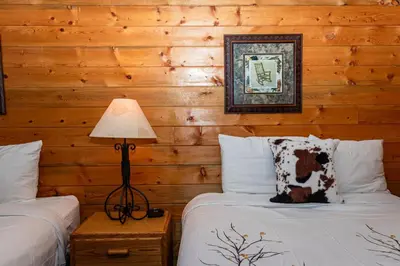 two beds in a room with wooden walls at Elk Run cabin steps to lake, In town, 5 min to RMNP in Grand Lake