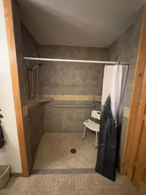 a bathroom with a shower with a bench and a shower curtain at Hummingbird Heaven Cozy Cabin 1 Block to Lake, located in Town in Grand Lake