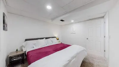 a white bedroom with a large bed with a purple blanket at Cozy Mountain-Inspired Lower Unit in Denver in Denver