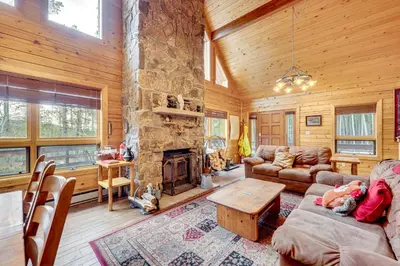 a living room with a stone fireplace in a log cabin at 4 Mi to RMNP Allenspark Cabin with Wraparound Deck! in Allenspark
