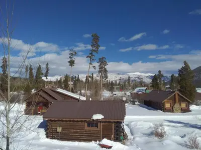 a log cabin in the snow with trees and mountains at Colorado Cabin Adventure in Grand Lake