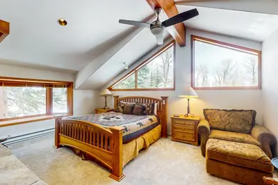 a bedroom with a bed and a chair and windows at Blue Riverfront Retreat in Silverthorne