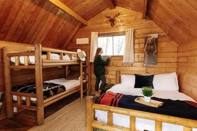 a woman standing in a log cabin bedroom with two bunk beds at Colorado Glamping Adventures in Golden Gate Canyon Park, in this Cute Cabin Rental in Black Hawk