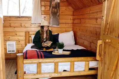 a woman sitting on a bed in a log cabin at Colorado Glamping Adventures in Golden Gate Canyon Park, in this Cute Cabin Rental in Black Hawk