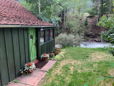 a green house with a door and flowers in a yard at Romantic Hideaway Cottage on Clear Creek in Georgetown, Colorado in Georgetown