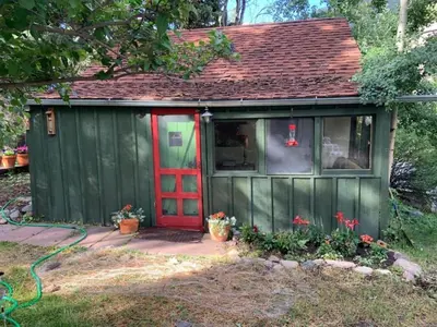 a green shed with a red door and flowers at Romantic Hideaway Cottage on Clear Creek in Georgetown, Colorado in Georgetown