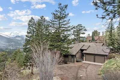 a house on a hill with mountains in the background at Montane Luxury Vacation Rental at Windcliff home in Estes Park