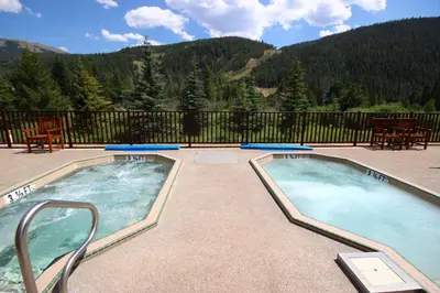 two hot tubs on a patio with mountains in the background at Hidden River Lodge 5965 by SummitCove Lodging in Keystone