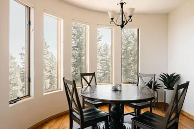 a dining room with a table and chairs and windows at Peaceful Getaway with Hot Tub - Views - Evergreen in Evergreen