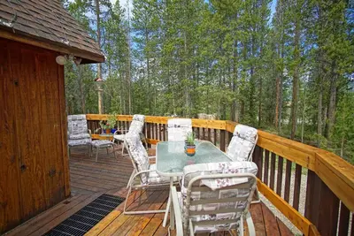 a wooden deck with a table and chairs on it at Pet Friendly, Firepit, Wrap around Porch, Close to Lake Granby and Highland Marina in Grand Lake