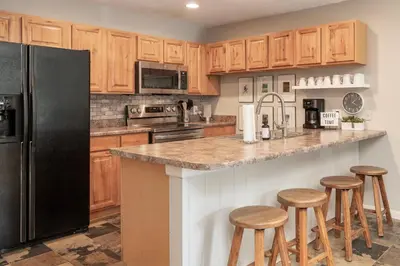 a kitchen with a black refrigerator and wooden cabinets at Versatile Rental, Firepit, Balcony with Grill and Outdoor Seating in Fraser