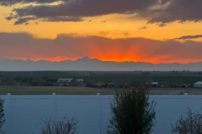 a sunset over a fence with mountains in the background at Private Hot Tub and Game Room Keenesburg Getaway! in Hudson