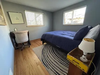 a bedroom with a bed and a chair and two windows at Crown Hill Gem - Hot Tub, Yard, Parking in Lakewood
