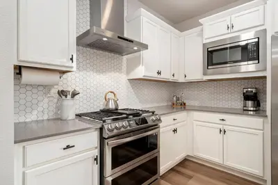 a kitchen with white cabinets and a stove at Mosaic Modern - Dog Friendly, Pool and King Suite in Fort Collins