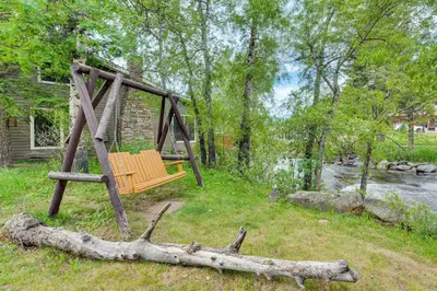 a wooden swing in a yard next to a river at Private Hot Tub - Riverfront Cabin In Estes Park! in Estes Park
