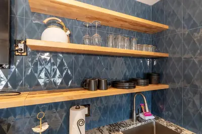 a kitchen with blue tiles and wooden shelves above a sink at Modern Getaway with Private Balcony in Denver