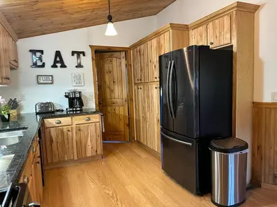 a kitchen with a black refrigerator and wooden cabinets at The Carriage House, Walk to River & Lake, In Town in Grand Lake