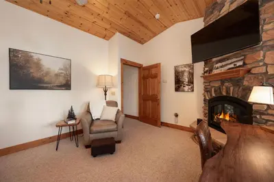 a living room with a stone fireplace and a chair at Beacon Landing Condo, Lakefront on Lake Granby, Luxurious Quality with Marina Right Outside in Grand Lake
