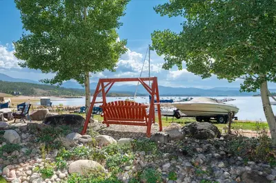a red bench sitting on a beach with a boat at Beacon Landing Condo, Lakefront on Lake Granby, Luxurious Quality with Marina Right Outside in Grand Lake