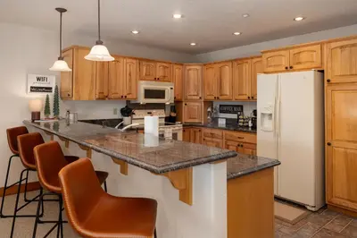 a kitchen with wooden cabinets and a white refrigerator at Beacon Landing Condo, Lakefront on Lake Granby, Luxurious Quality with Marina Right Outside in Grand Lake