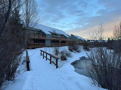 a building covered in snow next to a river at Condo 2BR on Winter Park Ski Bus Route for Christmas in Fraser