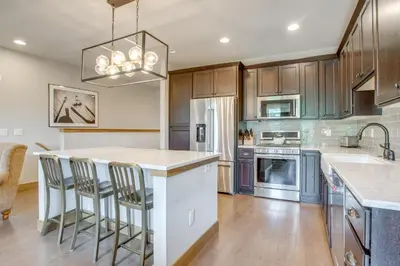 a kitchen with wooden cabinets and a island with bar stools at 2 Mi to Fraser River Trail Townhome with Hot Tub! in Fraser