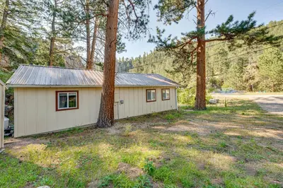 a small white building in a yard with trees at Hike, Fish and Relax Cabin 4 Mi to Lake Estes! in Drake