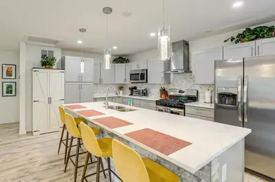 a kitchen with white cabinets and a large island with yellow chairs at Modern Wheat Ridge Home about 5 Mi to Dtwn Denver in Wheat Ridge