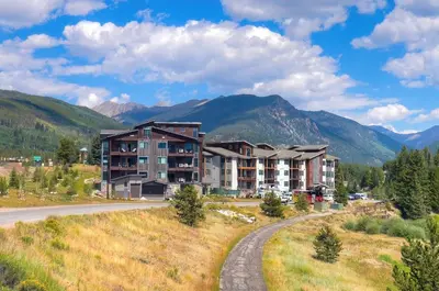 an apartment building on a hill with mountains in the background at Spacious and Luxurious 2BR Condo - Kids Ski Free condo in Keystone