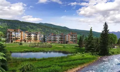 a resort with a pond and mountains in the background at Spacious and Luxurious 2BR Condo - Kids Ski Free condo in Keystone