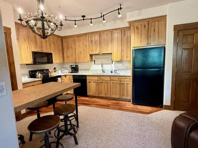 a kitchen with wooden cabinets and a black refrigerator at 2 BR Basecamp Bliss at Kicking Horse Near Ski Hill in Granby