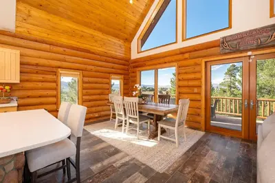 a dining room with a table and chairs and windows at Granby Panoramic Paradise! Hot tub and firepit! in Granby